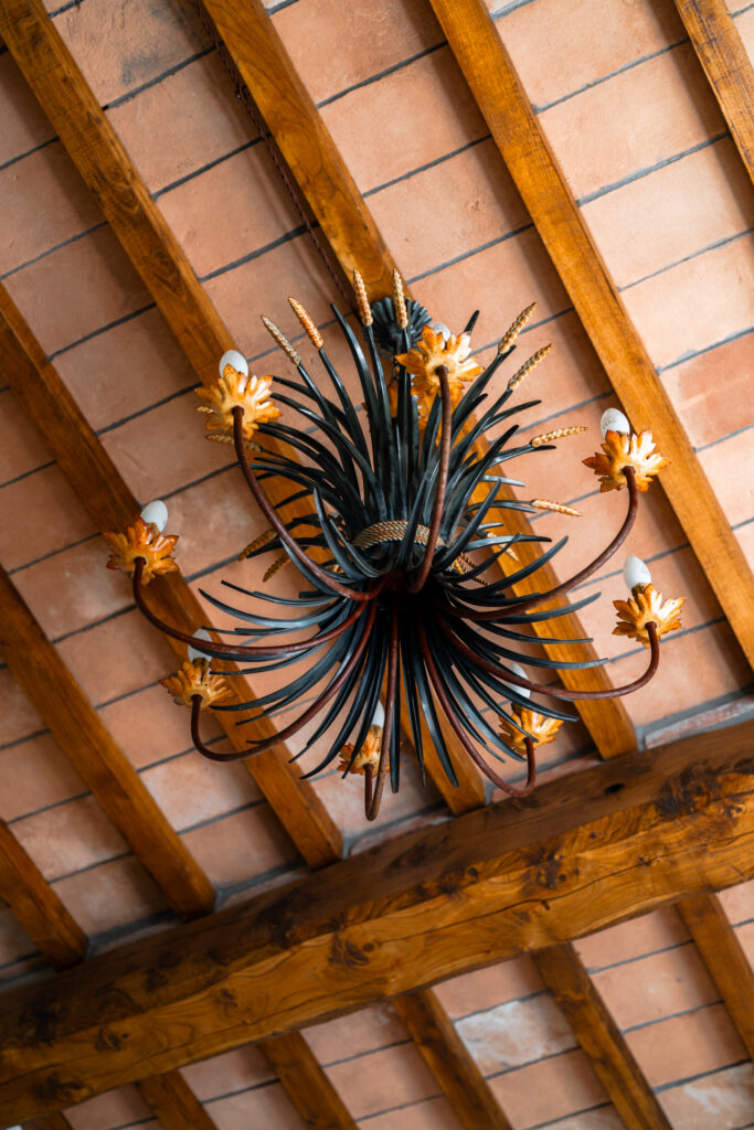 Detail of an artistic wrought-iron chandelier with floral design on a wooden beam ceiling at Villa MonteLandi in Tuscany — symbol of craftsmanship and style, Coco-Chanel