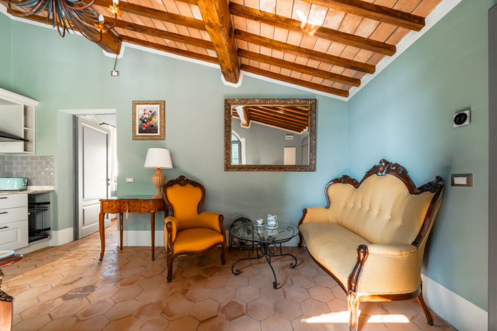 Bright living area at Villa MonteLandi in Tuscany with antique yellow armchairs, wooden beams, and mint green walls — elegant blend of tradition and comfort.