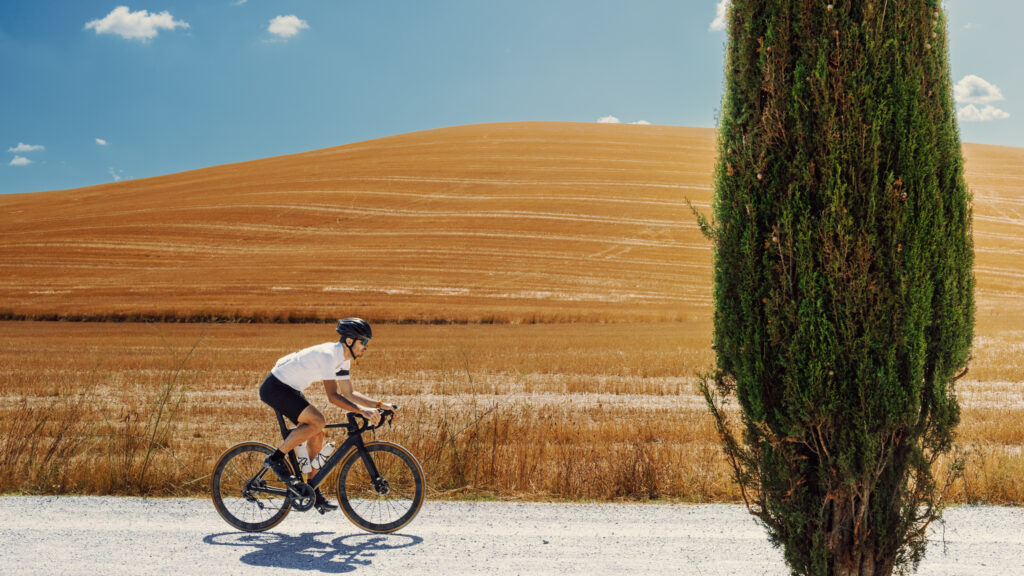 Guest cycling through a scenic dirt road surrounded by olive groves and Tuscan hills on a sunny day