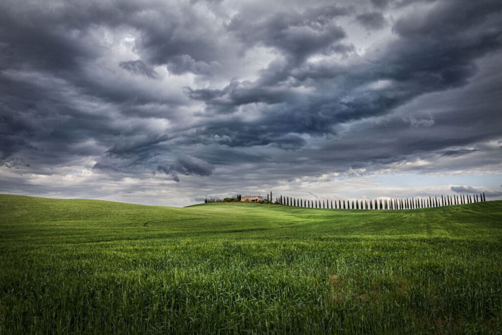 Poggio Covili cypress-lined road and farmhouse under dramatic sky in Val d’Orcia Tuscany near Villa Montelandi luxury villa