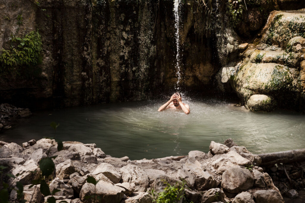 Man bathing under thermal waterfall at Bagni San Filippo hot springs, Val d’Orcia Tuscany