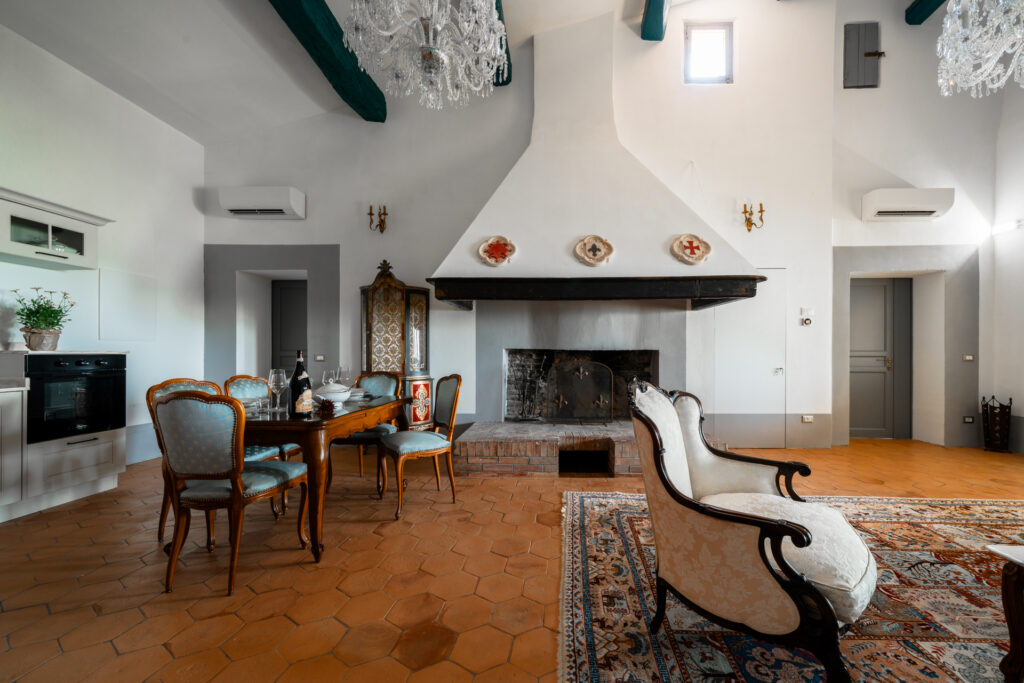 Elegant Tuscan dining room at Villa Montelandi with antique furniture, chandelier, and large fireplace, blending traditional charm with modern comfort.