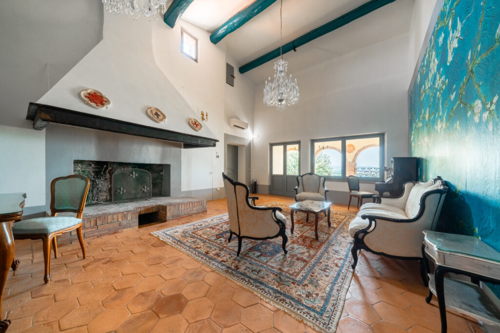 Spacious living area at Villa Montelandi featuring a grand fireplace, crystal chandeliers, and classic Tuscan decor with a view of the arches and hills.