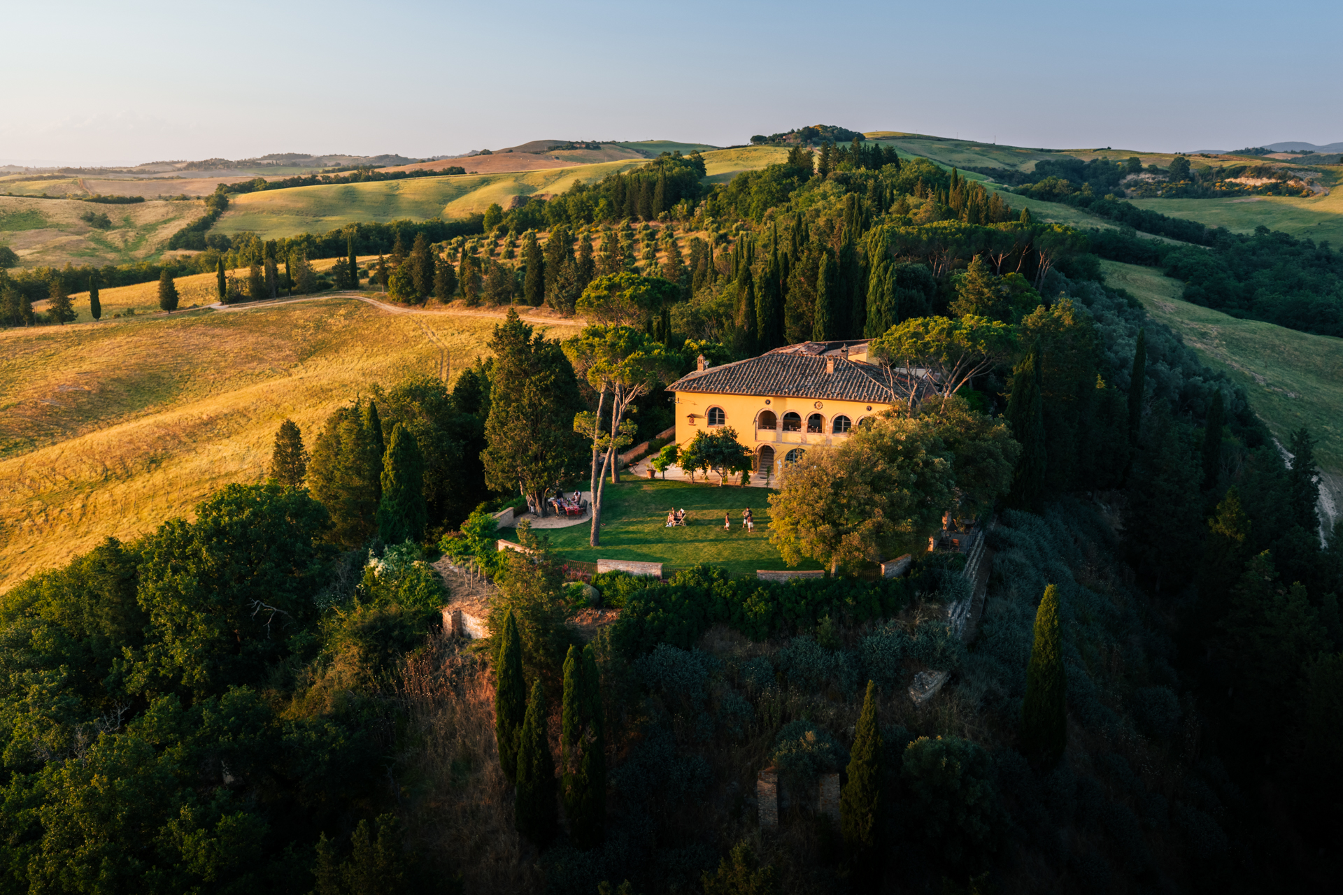 Exterior view of Villa Montelandi, a traditional Tuscan villa nestled in the rolling hills of Montalcino, Val d'Orcia, featuring a private pool, manicured garden, and panoramic countryside views.