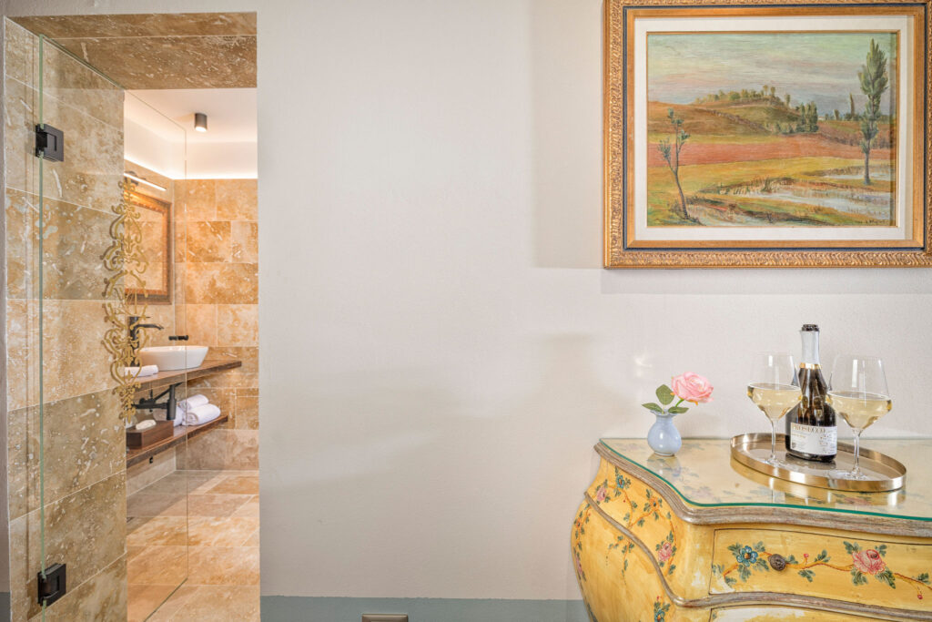 Detail from the Tramonto Toscano apartment at Villa Montelandi, featuring a hand-painted antique chest of drawers and a framed landscape painting inspired by the Tuscan countryside.