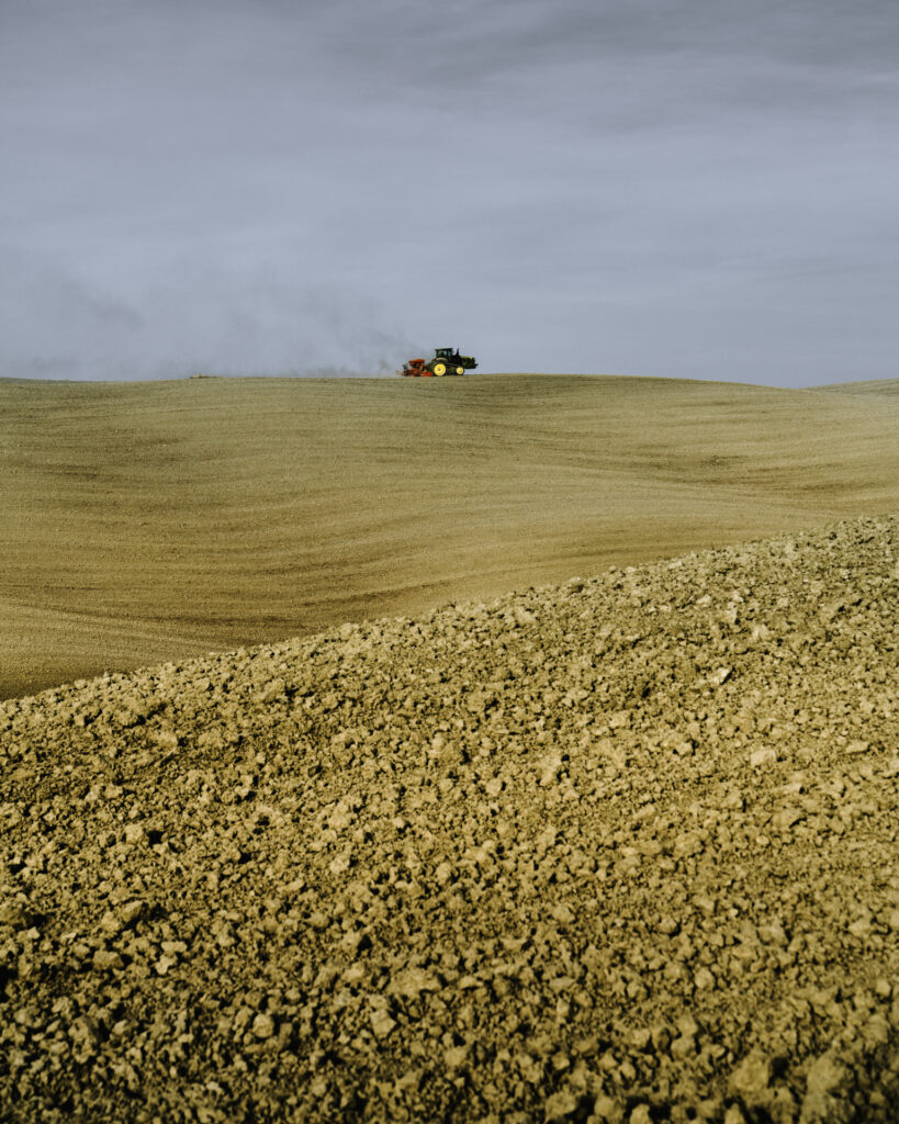 Farmer’s hands driving a tractor while working the land in the Crete Senesi, a UNESCO World Heritage landscape in Tuscany.