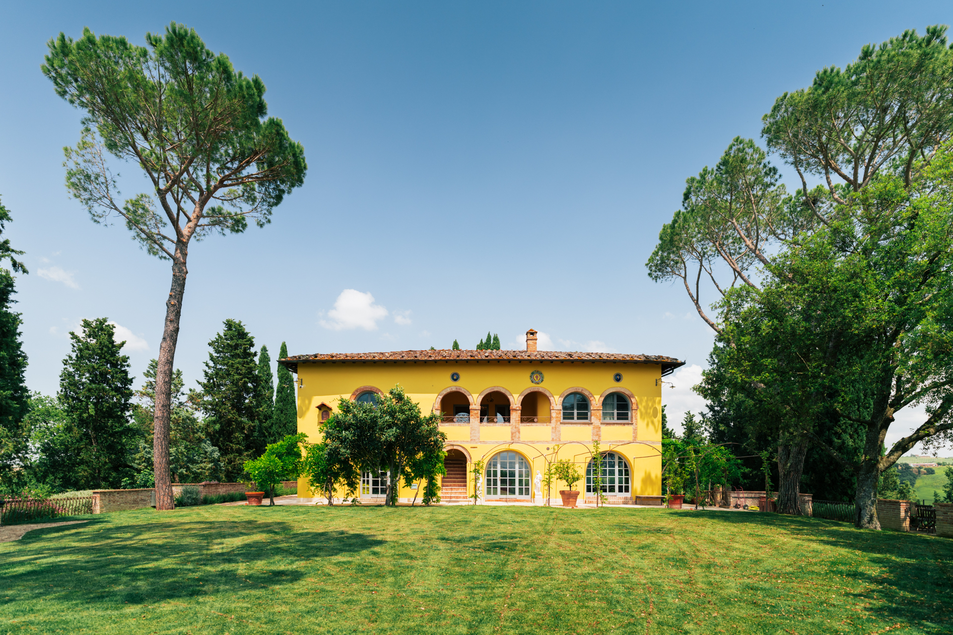 Main facade of Villa Montelandi yellow Tuscan villa with arches and terrace Val d’Orcia