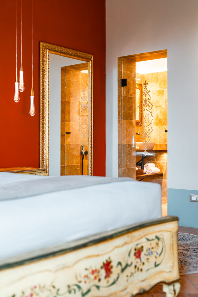 Luxury suite in Tuscany at sunset, featuring soft chandelier lighting, elegant bathroom details, and a refined bed with a romantic atmosphere.