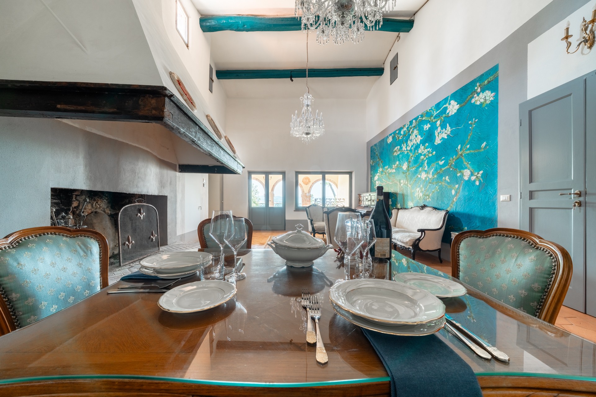 Elegant dining area at Villa MonteLandi in Tuscany with vintage furniture, large fireplace, and crystal chandeliers — a refined atmosphere combining art, tradition, and Tuscan charm.