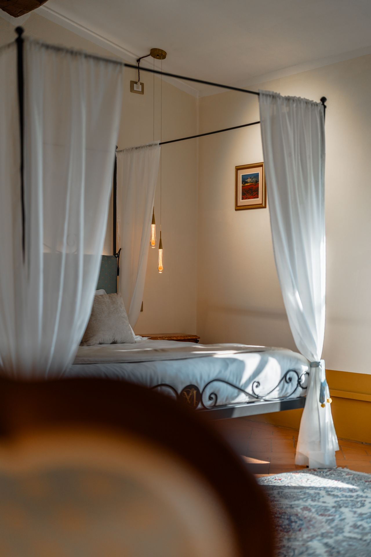 Elegant bedroom at Villa MonteLandi in Tuscany with wrought-iron canopy bed, soft natural light, and refined minimalist decor — combining comfort and Tuscan authenticity.