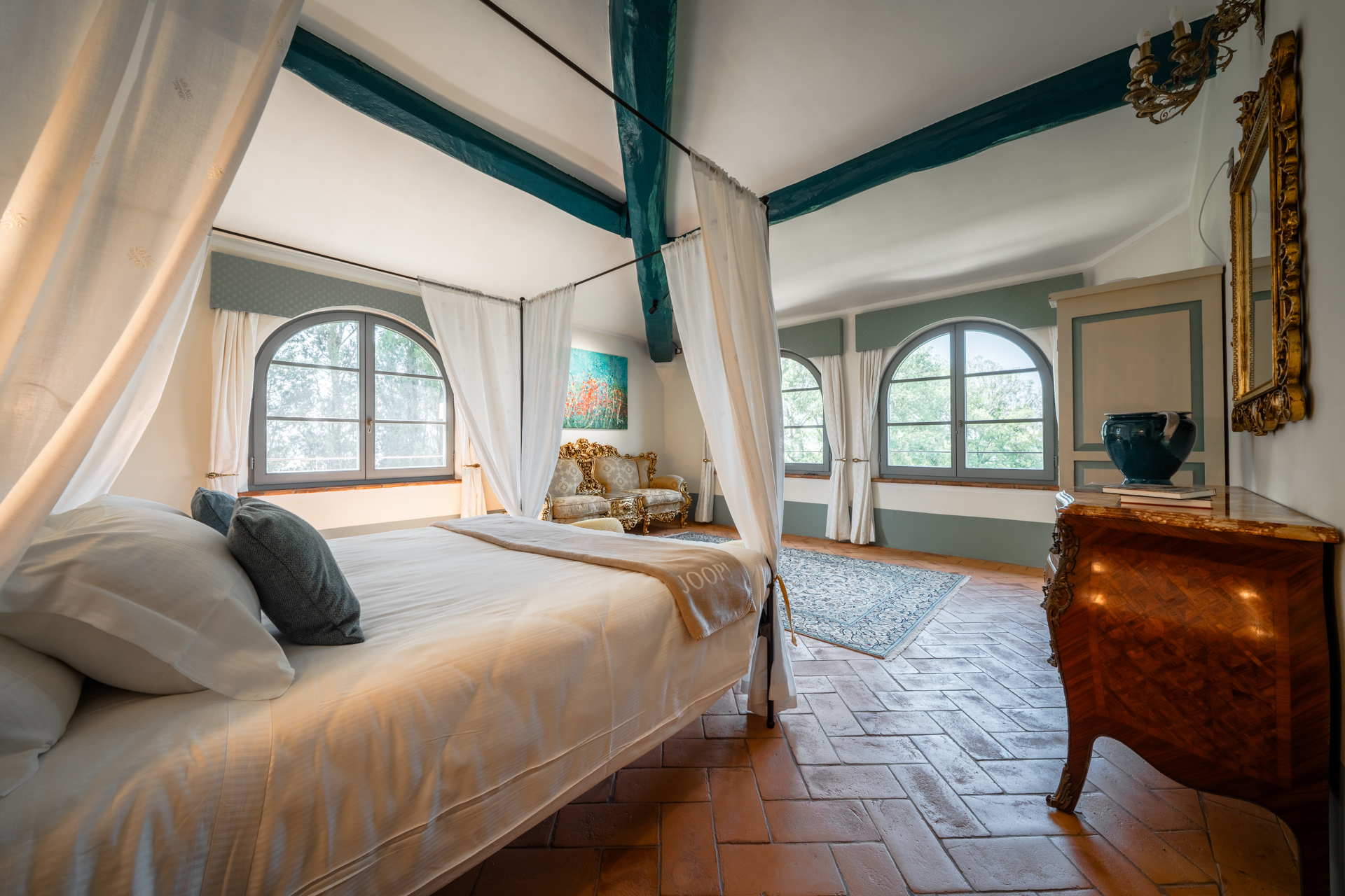 Spacious suite at Villa MonteLandi in Tuscany with four-poster bed, terracotta floors, and arched windows overlooking the park — a blend of elegance, light, and authentic Tuscan charm.
